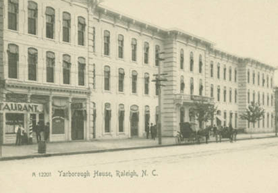 Un largo edificio blanco de tres pisos al lado de un restaurante. Delante hay un carruaje. El texto de la imagen dice &quot;Yarborough House Raleigh, N.C.&quot;