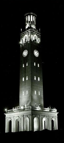 A large tower, illuminated at night. A clock adorns the two visible sides.