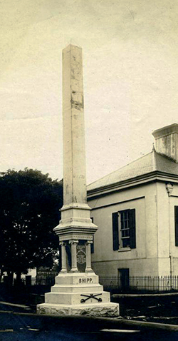 The monument to William Ewen Shipp in Charlotte. Image from the North Carolina Museum of History. A large stone obelisk next to a building.