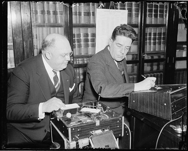 &quot;Demonstrates new signature machine to house member. Washington, D.C., March 18 [1938]. The latest is the automatic electric signature machine invented by Glenn W. Watson, (left) who is shown in this picture demonstrating it to Rep. Lindsay C. Warren of North Carolina.&quot; Presented on Library of Congress.