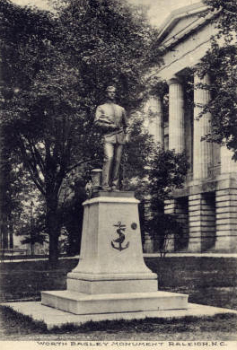 A statue of Badgley. He is wearing a military uniform and is posed. Statue on a stone plinth, and a Classical style building marks the background.
