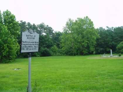 A large metallic marker in front of field circled by trees.  Marker reads: &quot;BATTLE OF ROCKFISH, The British under Major Craig defeated the North Carolina Militia, Aug. 2, 1781, 300 yards S.E.&quot;