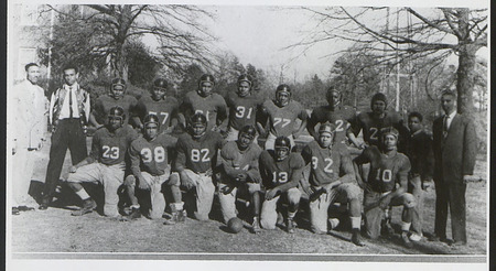 The Palmer football team of fourteen Black men pose some kneel and other stand behind those kneeling