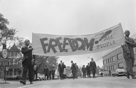 Several black men walk down a street with a sign reading Freedom for all People