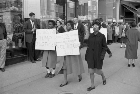 Black women walk down a sidewalk with protest signs in front of store