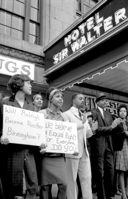 Several black men and women stand outside a business with protest signs