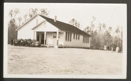 A large group of students stands in front of a large white school building