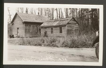 One man stands in front of two wooden buildings