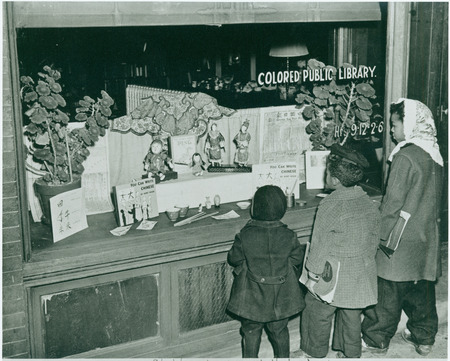 Black children hold books and look at a window display for Asheville's African American library