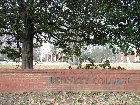 A low brick wall reading Bennett College, brick buildings are visible over the top of the wall