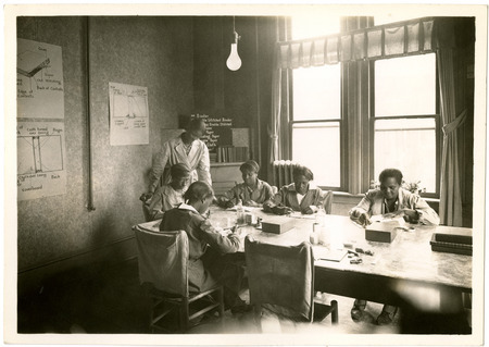 Six Black women sit around a table working to repair books