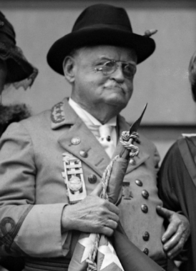 &quot;General&quot; Julian Shakespeare Carr in uniform, November 22, 1923. Image from the Library of Congress. The photograph shows an older man, with glasses and a mustache, wearing military dress and holding a flag. He appears to be with other people who are not in full view in the photo. This photograph of Carr has been excerpted from the original which shows Carr standing with two women and a man.