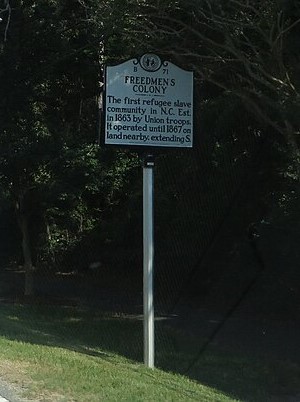 Photograph the North Carolina Highway Historical marker dedicated to the Freedmen's Colony. It is located in Manteo, North Carolina and reads: The first refugee slave community in N.C. established in 1863 by Union troops. It operated until 1867 on land nearby and extending south