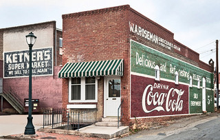 A brick building. A striped awning is over the door and windows into the building. &quot;Ketner's Super Market&quot; and a Coca Cola ad are painted on the building walls.